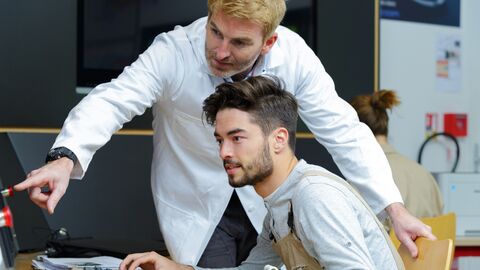 Formateur expliquant un point à un étudiant en alternance devant un ordinateur
